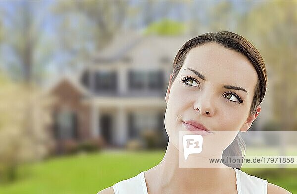 Nachdenkliche hübsche gemischtrassige Frau vor einem Haus  die nach oben und zur Seite schaut