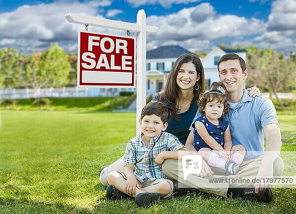 Junge Familie mit Kindern vor maßgeschneidertem Haus und Immobilienschild zu verkaufen