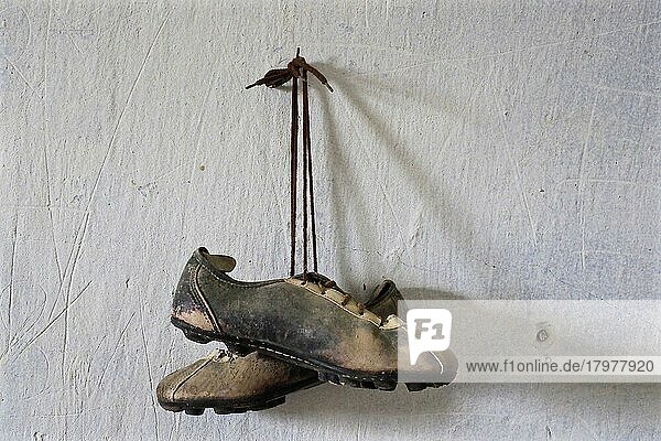 Paar von Fußballschuhen hängt an Nagel  Herren-Sportschuh  maroder Schuh aus Leder  verrotteter Schuh  Schuhwrack  vergammelter Treter  ausgelatschter Schuh  abgetragener Schuh  alter Schuh