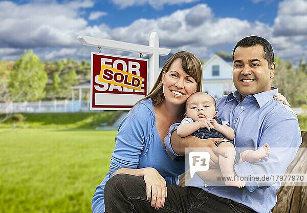 Glückliche gemischtrassige junge Familie vor einem verkauften Haus zu verkaufen Immobilienschild und Haus