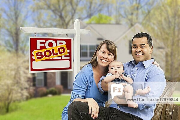 Glückliche gemischtrassige junge Familie vor einem verkauften Haus zu verkaufen Immobilienschild und Haus