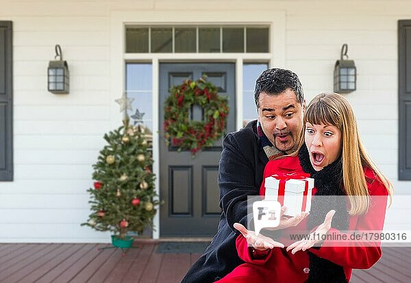 Junges gemischtrassiges Paar tauscht auf der Veranda eines weihnachtlich geschmückten Hauses Geschenke aus