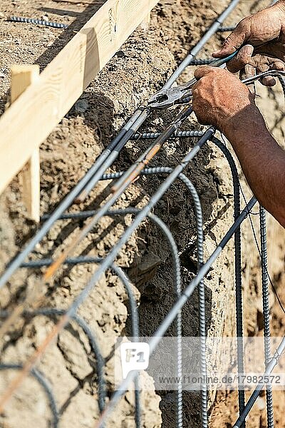 Arbeiter  der mit einer Drahtzange auf der Baustelle Bewehrungsstäbe sichert