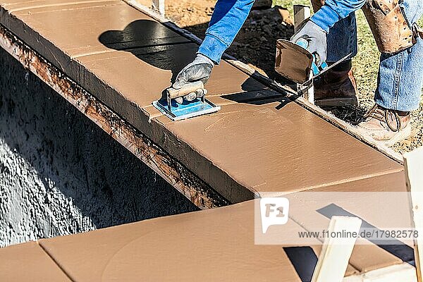 Ein Bauarbeiter arbeitet mit einer Handfräse auf nassem Zement und formt eine Abdeckung für einen neuen Pool