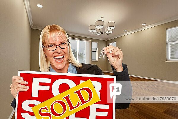 Attraktive junge Frau mit neuen Schlüsseln und verkauftem Immobilienschild im leeren Raum eines Hauses