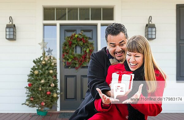 Junges gemischtrassiges Paar tauscht auf der Veranda eines weihnachtlich geschmückten Hauses Geschenke aus