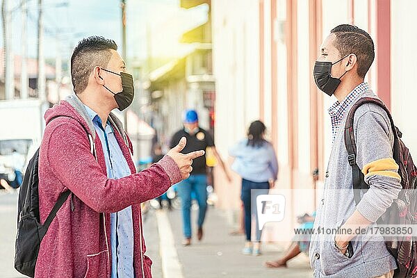 Zwei junge Leute mit Maske unterhalten sich im Freien  zwei Freunde mit Gesichtsmaske unterhalten sich  Konzept des Gesprächs und der sozialen Distanz