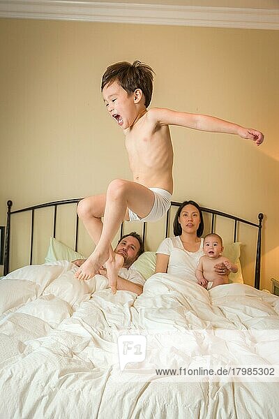 Junge gemischtrassige chinesischer und kaukasische Jungen springen im Bett mit seiner Familie