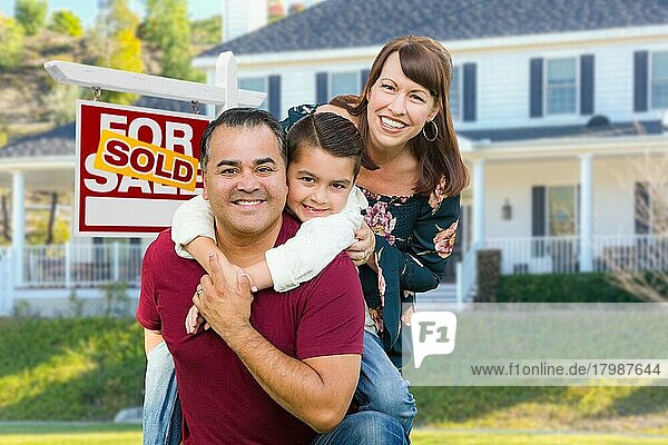 Glückliche gemischtrassige Familie vor einem Haus und einem Immobilienschild  das zum Verkauf steht