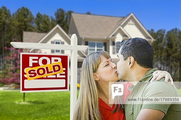 Glückliches gemischtrassiges Paar vor einem verkauften Haus zu verkaufen Immobilienschild und Haus