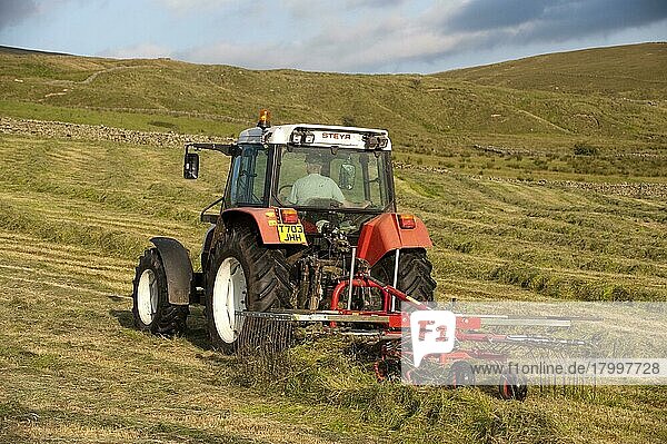 Styer 9078 Traktor rudert auf einem Bergbauernhof Gras hoch  um Großballen-Silage herzustellen  England  Juli