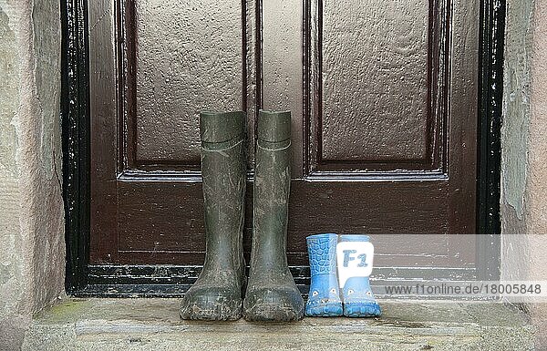Zwei Paar Gummistiefel  ein Paar Kinder- und ein Paar Herrenstiefel  vor der Tür des Bauernhauses  Whitewell  Lancashire  England  Dezember