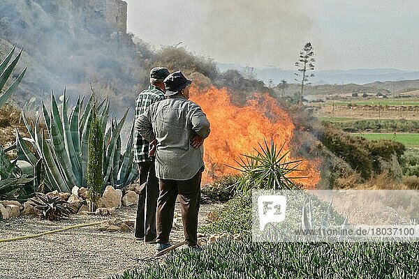 Old couple observes bush fire in Mediterranean garden  fire hazard  Grima  Andalucia  Spain  Europe