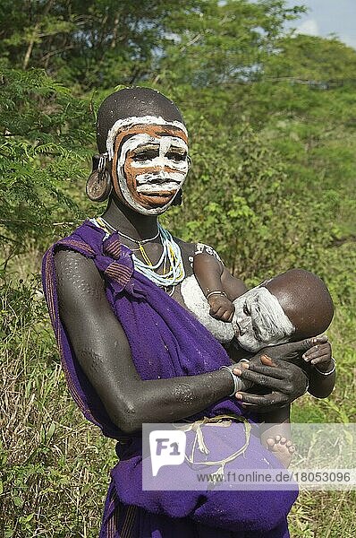 Surma-Frau mit Körperbemalung und Ohrenplatte  Gesichtsbemalung  saugendes Baby  Kibish  Omo Tal  Äthiopien  Afrika