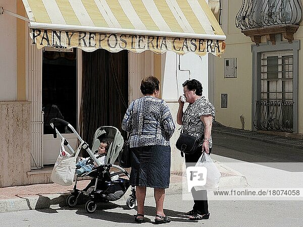 Conversation of two elderly woman on the street with baby in pram  customers in front of shop  Andalusia  Spain  Europe