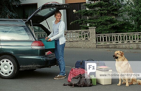 Mischlingshund neben Frau  die Auto für Reise packt  Gepäck  Deutschland  Europa