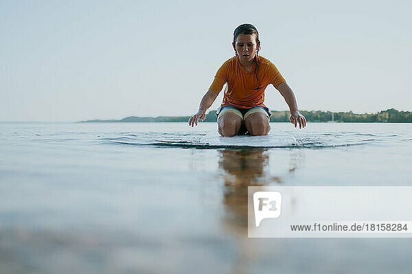 Low angle view of boy kneeling on paddle board paddling with hands
