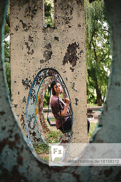 Junge Frau schaukelt auf einem verlassenen Spielplatz im Sommer