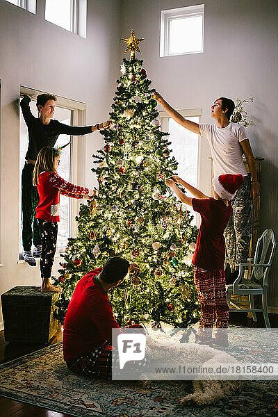 Familie schmückt Weihnachtsbaum mit Ornamenten im Haus