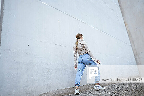 Girl in a blue pants stretching and dancing against grey wall