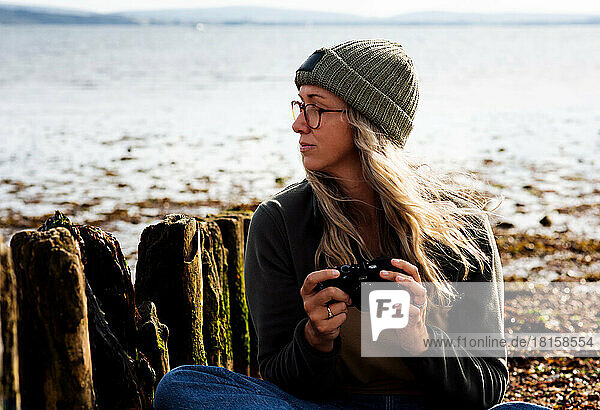 woman looking thoughtful whilst taking photos at the beach