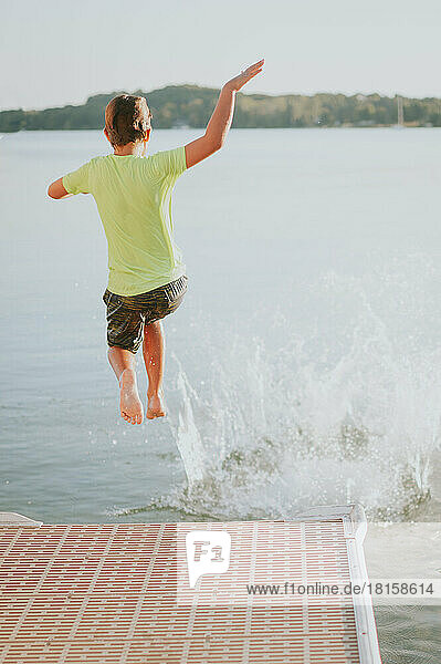Junge in grünem Schwimmshirt springt vom Steg in den See und spritzt darunter