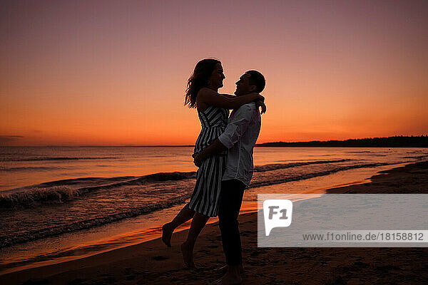 Silhouette eines jungen Liebespaares  das sich am Strand umarmt  während