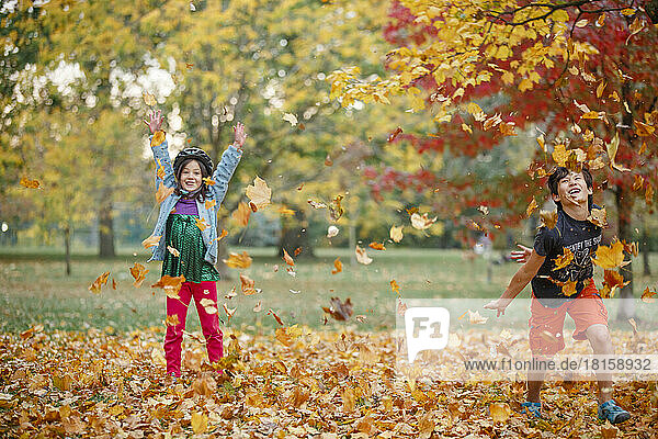 Zwei glückliche Kinder spielen zusammen in einem Haufen Herbstblätter