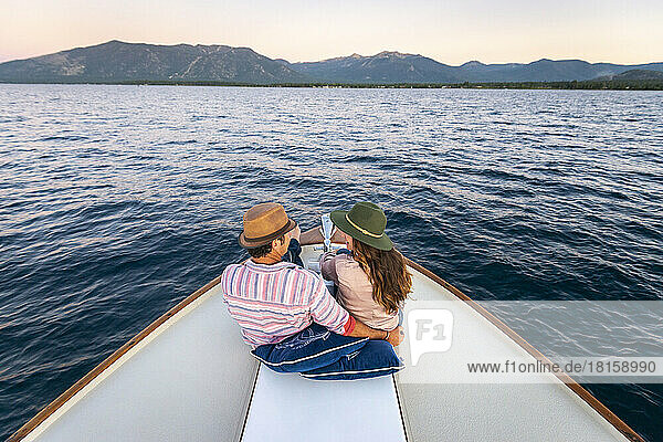 A couple sits on the bow of a yacht as they cruise during sunset.