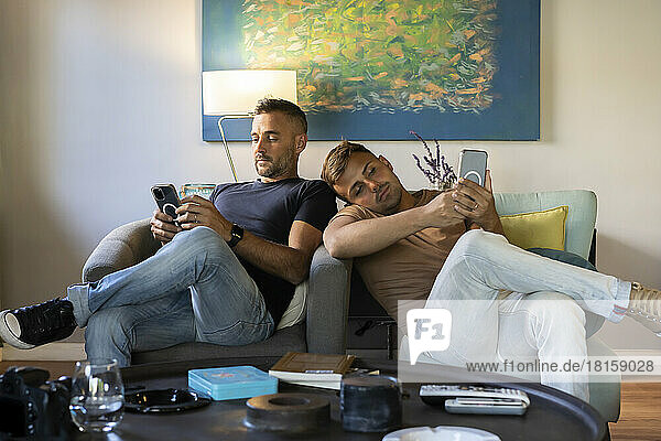 Homosexuelles Paar  das sich auf der Couch entspannt und Smartphones benutzt