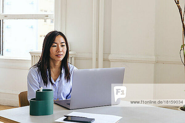 Female entrepreneur using laptop on desk in creative office