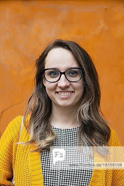 Ein Mädchen mit Brille auf einem orangefarbenen Hintergrund lächelt