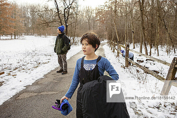 Ein Junge in Winterkleidung geht mit seiner Familie auf einem Waldweg spazieren