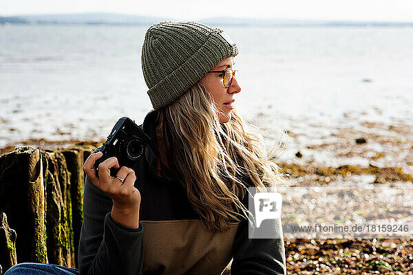 Frau sitzt am Strand und hält ihre Kamera an einem windigen Tag