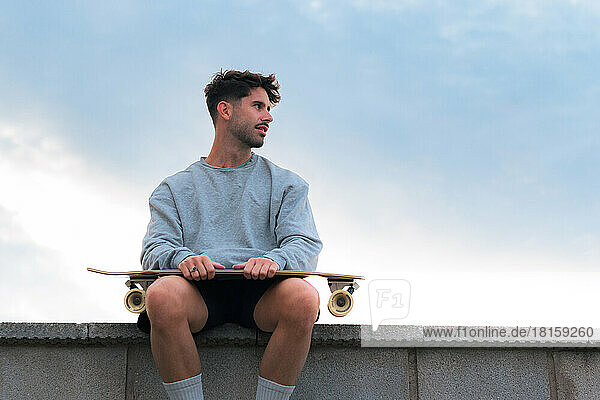 Young man sitting with a skateboard in a cloudy day at sunset