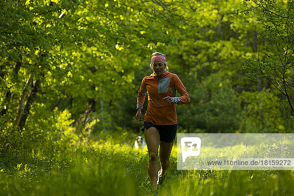 woman running in a green field in the forest with orange jacket