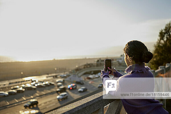 Rückansicht einer Frau  die mit ihrem Smartphone den Sonnenuntergang fotografiert
