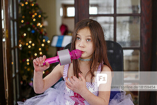 An earnest girl in tutu sings into a pink microphone at home