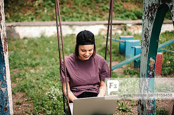 Glückliche junge Studentin mit Laptop auf einer Schaukel sitzend