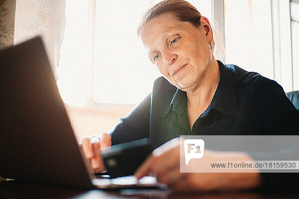 Ältere Frau mit Laptop und Kreditkarte beim Online-Shopping