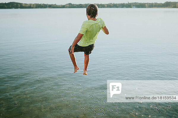 Full body view of boy in a midair jump above a lake for swimming