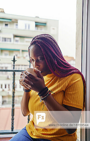 Afroamerikanische Frau trinkt Kaffee am Küchenfenster sitzend