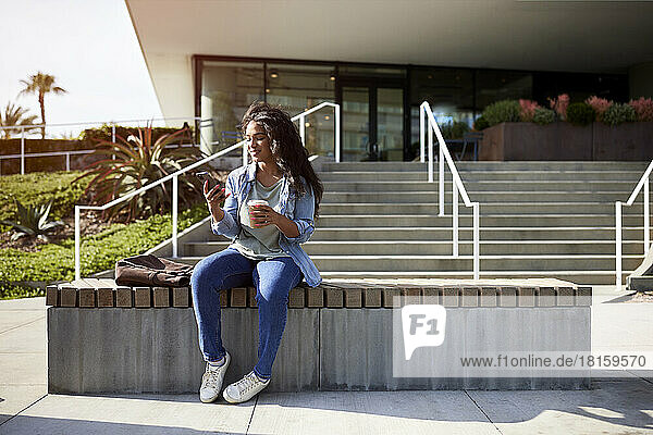 Lächelnde Frau  die ein Smartphone benutzt  während sie auf einer Bank sitzt