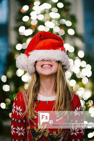 Blondes Kind lächelt mit Weihnachtsmannmütze vor dem Weihnachtsbaum