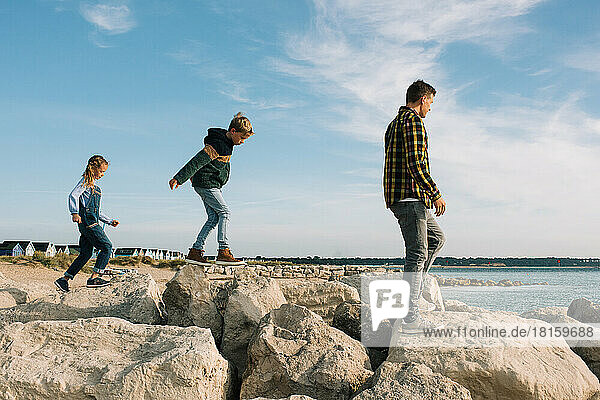 Vater und seine Kinder spazieren auf den Felsen am Strand