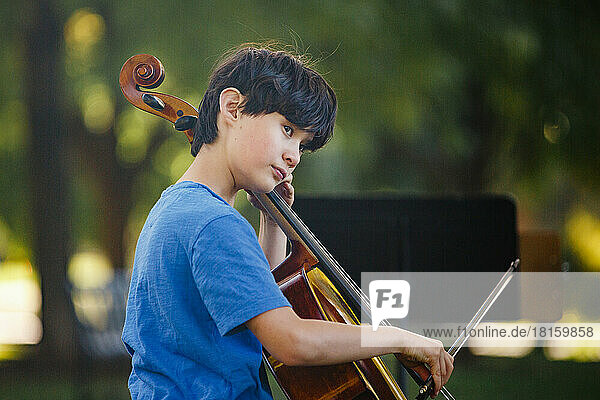 Ein schöner Junge spielt Cello im Park