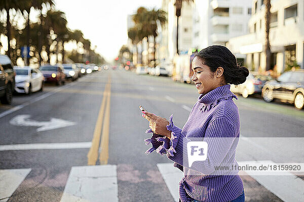Glückliche Frau benutzt ihr Smartphone beim Überqueren der Straße