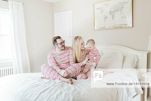 Kaukasische Eltern und Kleinkind im Weihnachtspyjama auf dem Bett.