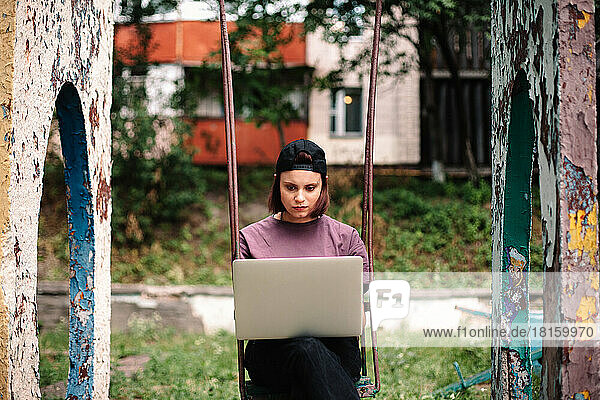 Seriöse junge Studentin mit Laptop auf einer Schaukel sitzend