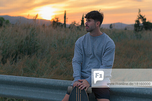 Porträt eines jungen Mannes mit einem Skateboard bei Sonnenuntergang